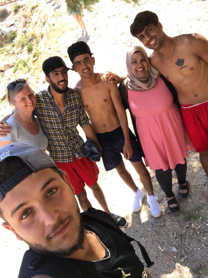 A group of six people, some shirtless and others dressed casually, pose closely together for a selfie outdoors on a sunny Day 2 in Chios Island, Greece. | Support refugees across Europe in Greece, France, the UK and the Balkans