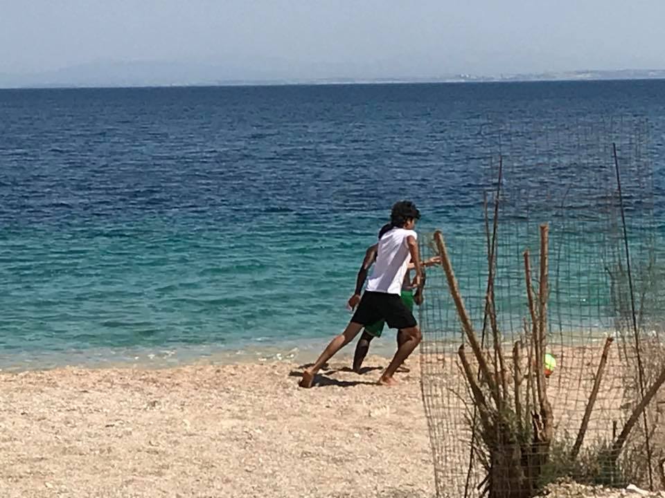 Two people play soccer on a sandy beach near the shoreline on Day 2 of their trip to Chios Island, Greece, with the blue ocean and distant land visible in the background. | Support refugees across Europe in Greece, France, the UK and the Balkans