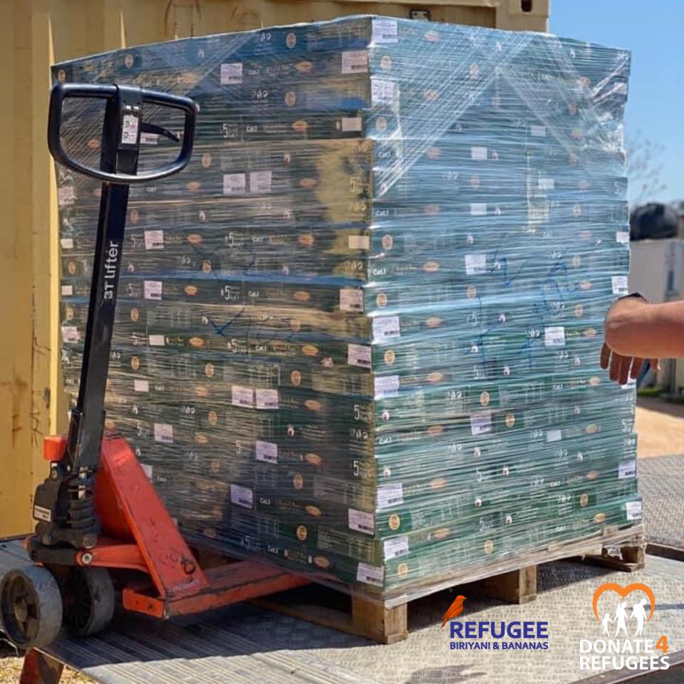 A pallet stacked with boxes, wrapped in plastic, sits on a pallet jack in Chios, Greece. Refugee Biriyani & Bananas and Donate 4 Refugees logos appear in the bottom right corner—essential aid during Ramadan and the COVID lockdown. | Support refugees across Europe in Greece, France, the UK and the Balkans