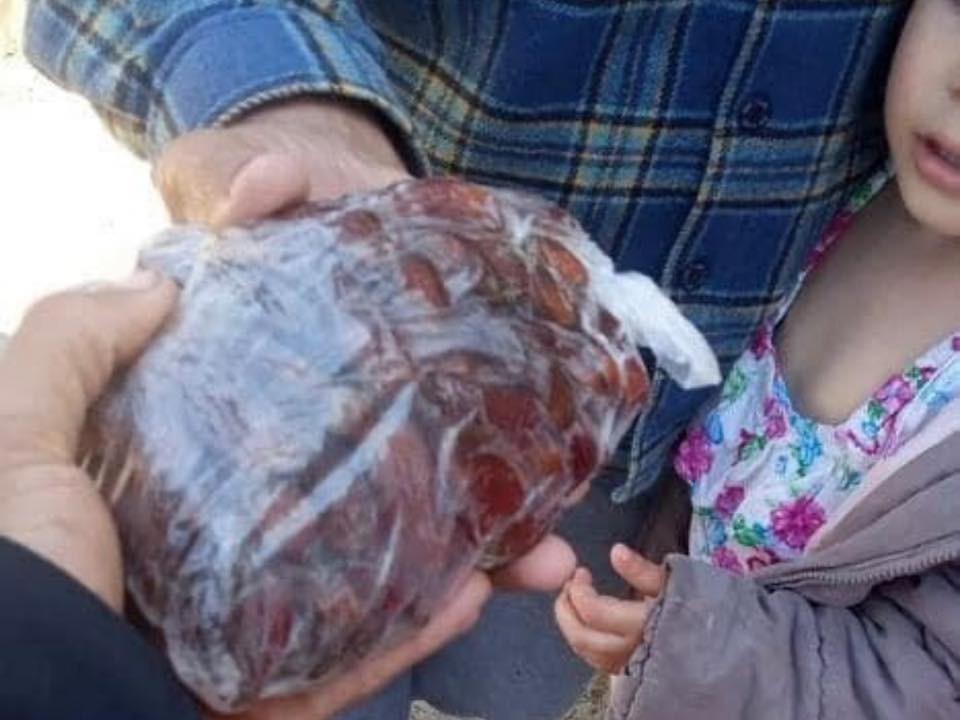 A person hands a plastic bag filled with dates to another during Ramadan, while a child stands nearby—a simple gesture reminiscent of togetherness even during the COVID lockdown. | Support refugees across Europe in Greece, France, the UK and the Balkans