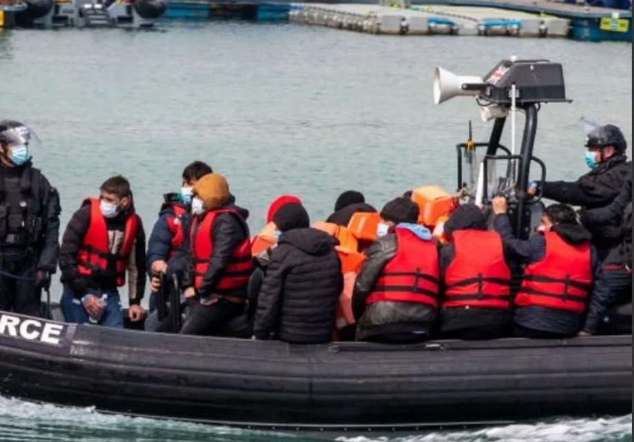 A group of people in life jackets on an inflatable boat accompanied by uniformed officers near a dock. | Support refugees across Europe in Greece, France, the UK and the Balkans