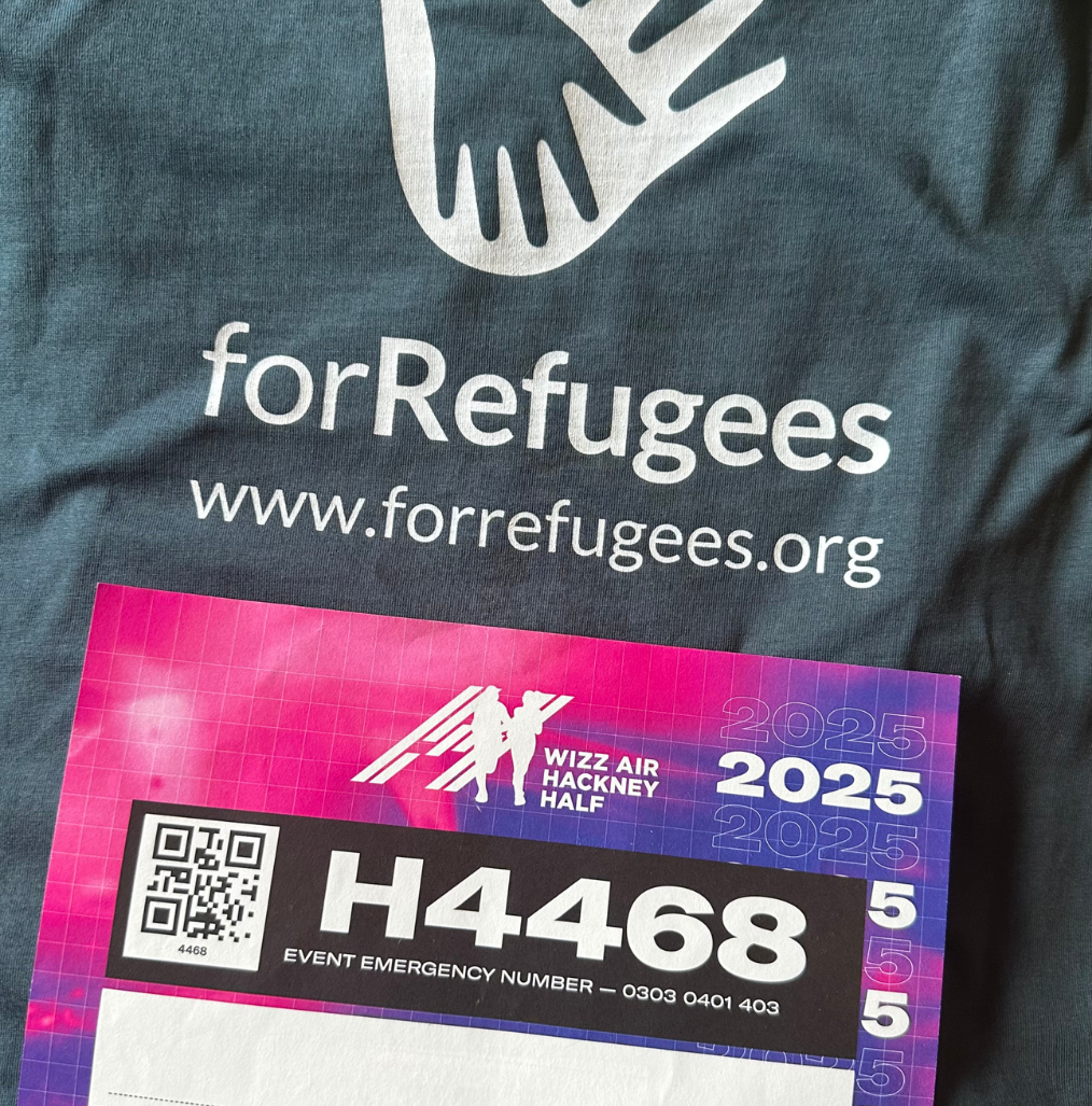 A race bib for the 2025 Wizz Air Hackney Half with the number H4468 rests on a "forRefugees" t-shirt displaying the website forrefugees.org. | Support refugees across Europe in Greece, France, the UK and the Balkans