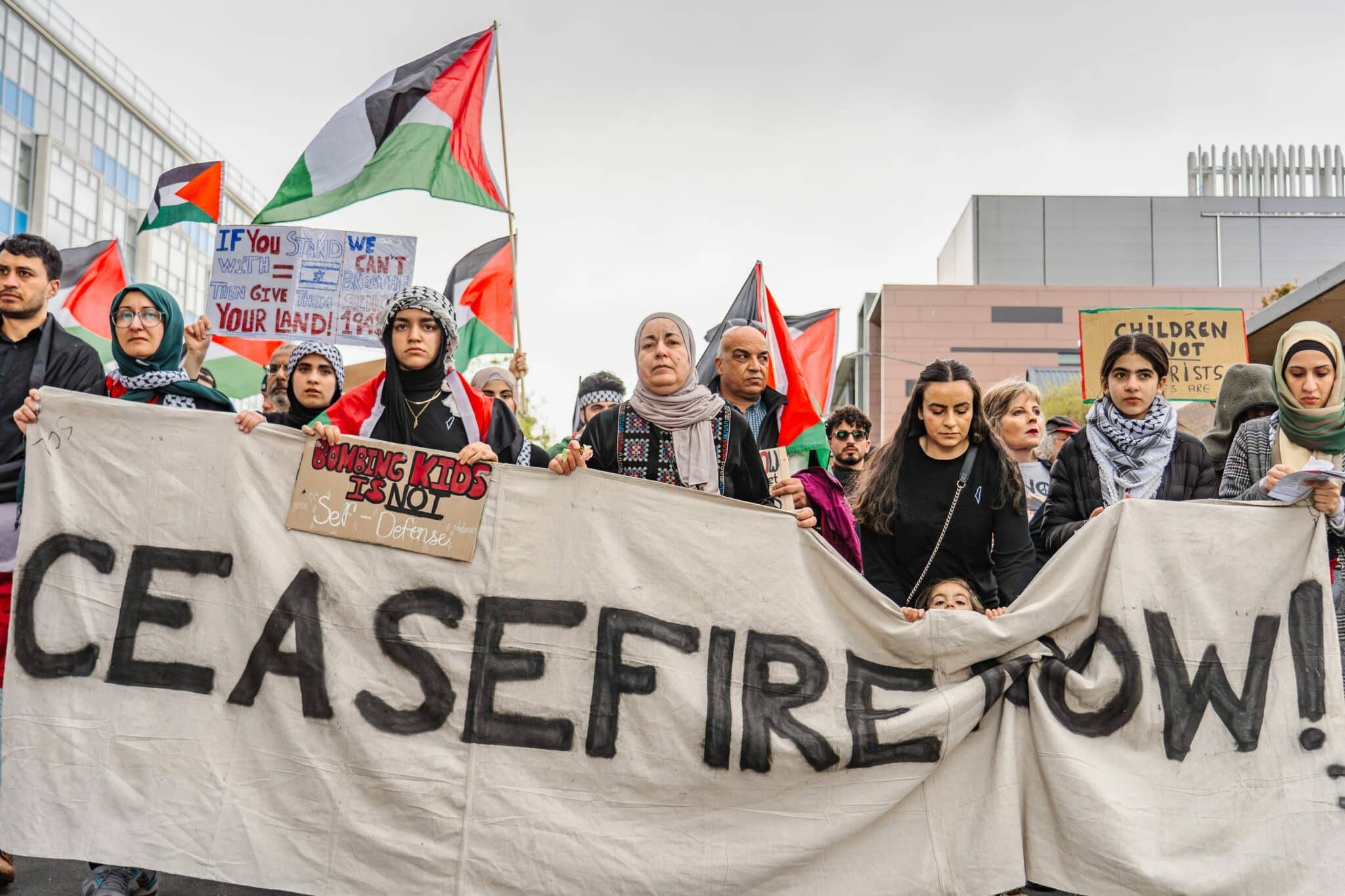 A group of protesters hold a large banner reading “CEASEFIRE NOW!” and display signs and Palestinian flags at a Gaza march, joining the Global March to Gaza demonstration. | Support refugees across Europe in Greece, France, the UK and the Balkans