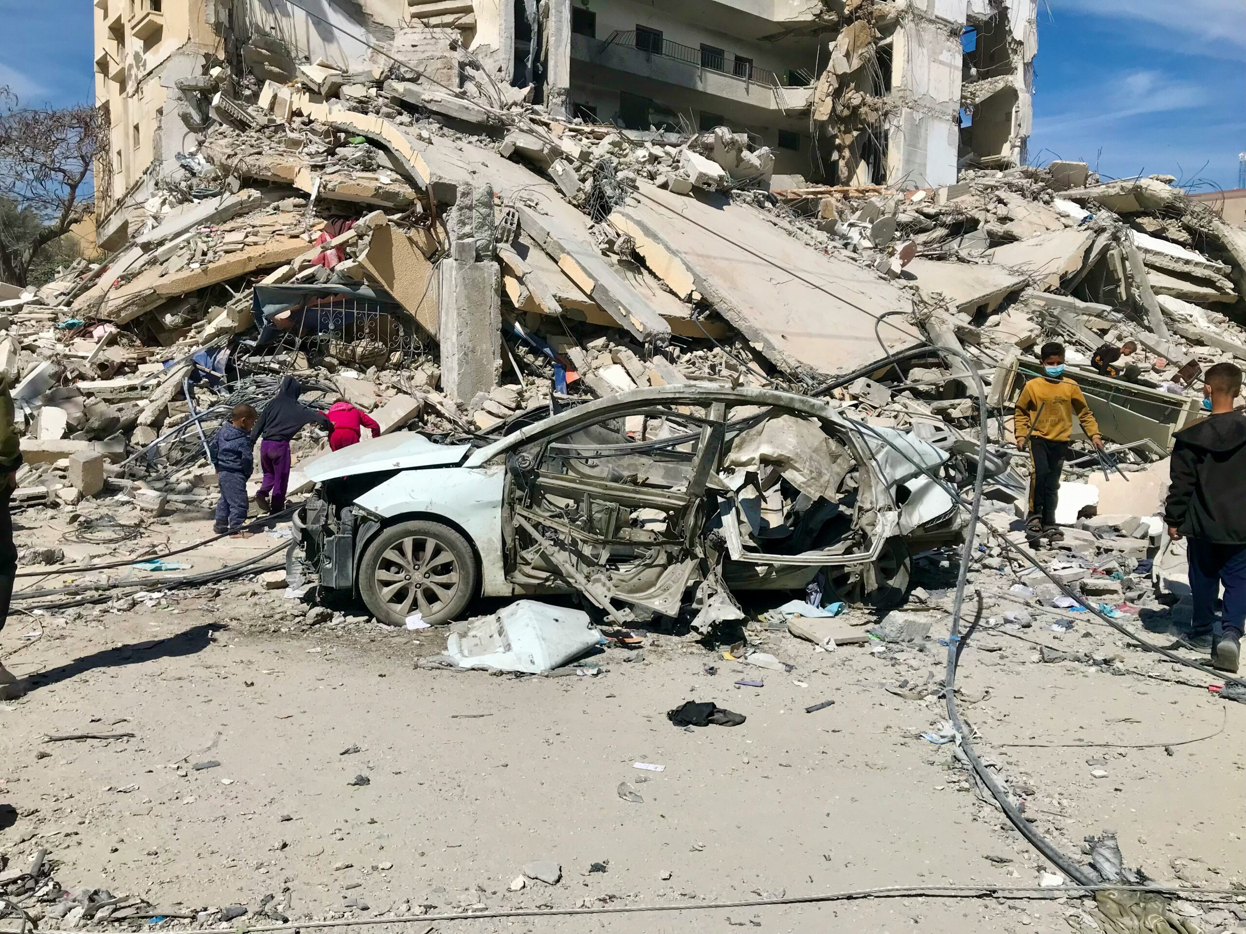 emad-el-byed-G1ocCKhX4Rs-unsplash A severely damaged car sits in front of a collapsed building as refugees walk among the rubble and debris, capturing the toll of the war in Gaza. | Support refugees across Europe in Greece, France, the UK and the Balkans